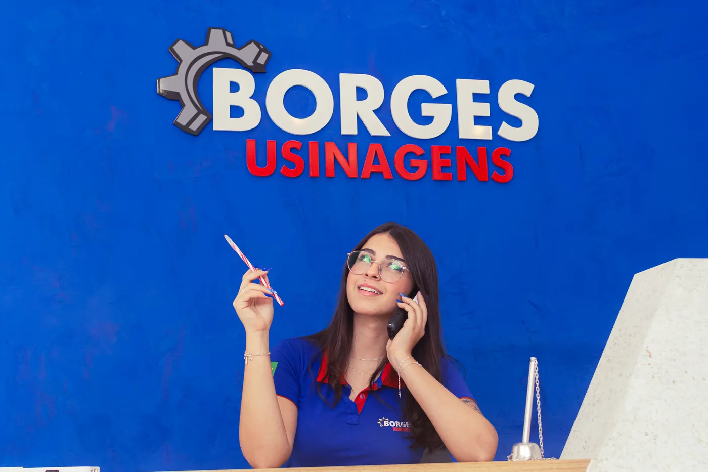 Atendente da Borges Usinagens falando ao telefone em frente ao painel da marca